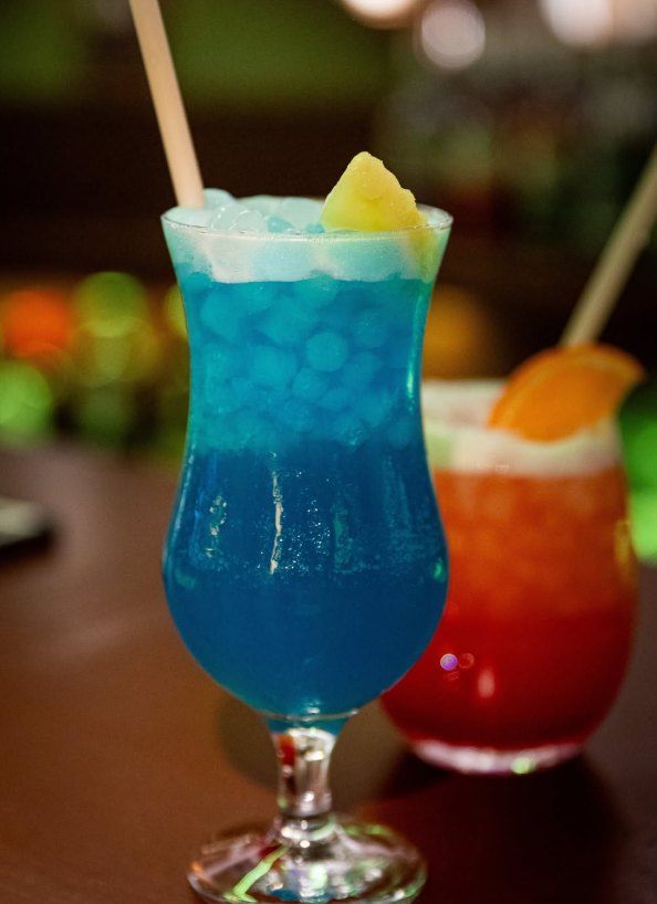 Cóctel azul con piña y cóctel rojo con naranja sobre la barra de La Playa Chipiona